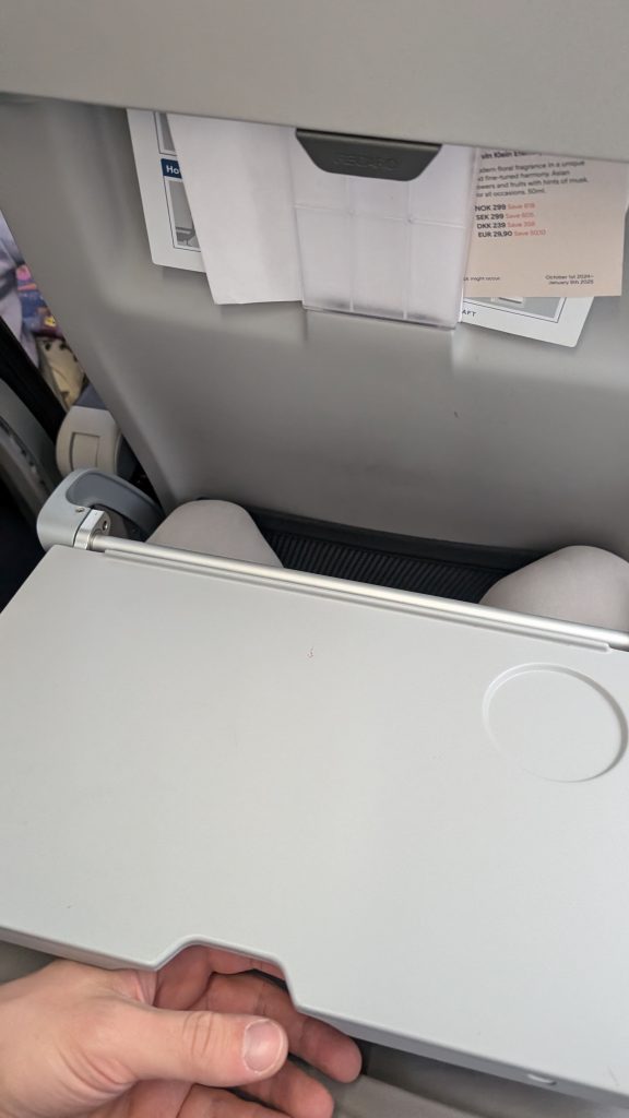 Heruntergeklappter Flugzeugtisch mit Getränkevertiefung und Sitzmagazin im Hintergrund
