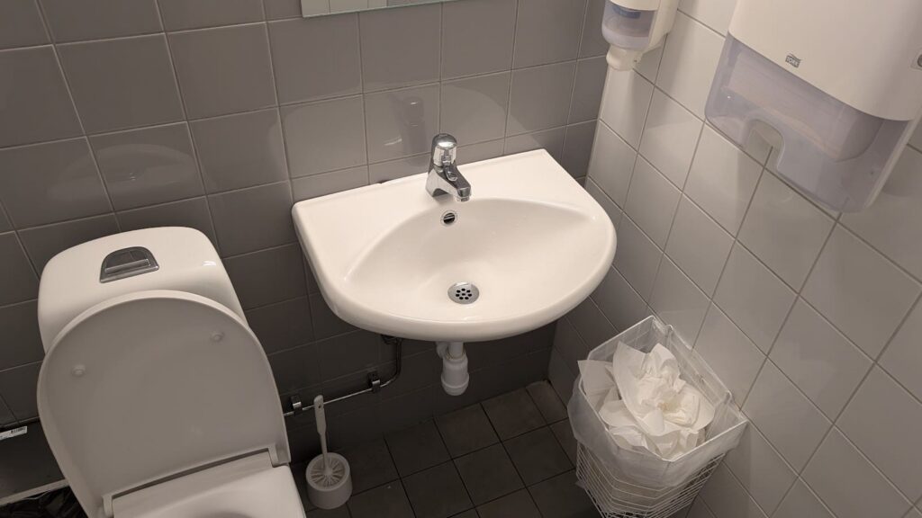 Weisses Waschbecken und Toilette im gefliesten Waschraum der Pearl Lounge